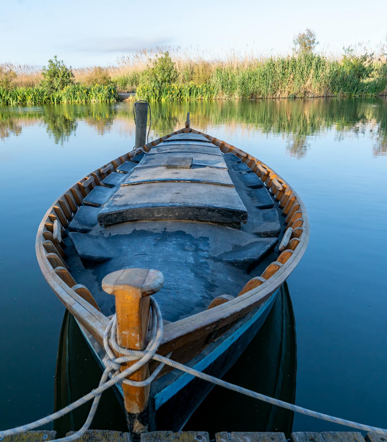 Wooden boat floating on a calm lake surrounded by green reeds