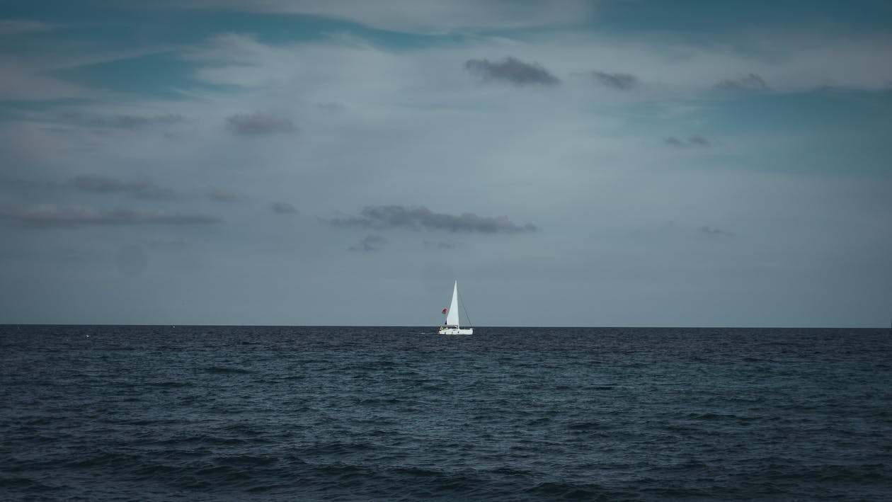 Lone sailboat on a wide blue ocean under cloudy sky
