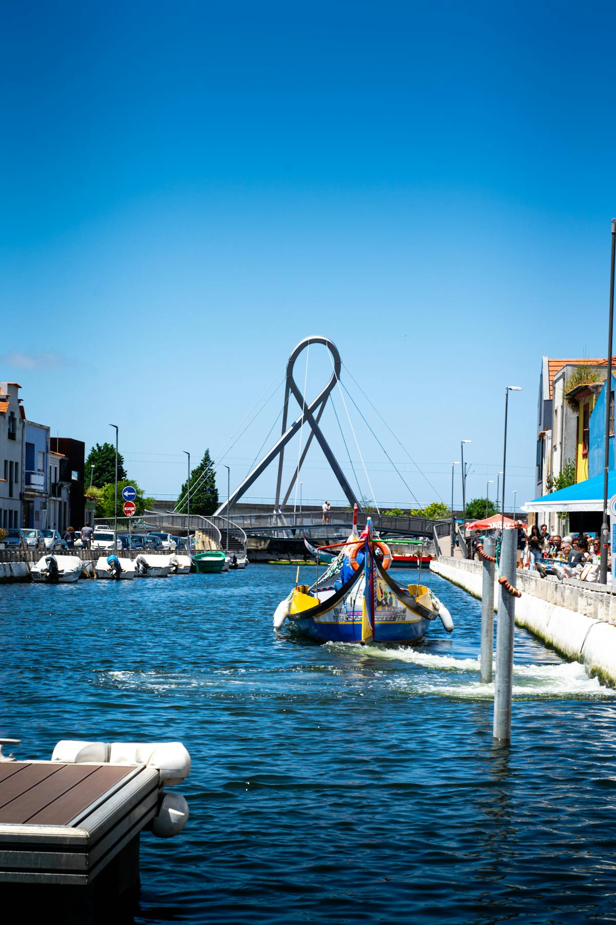 A colorful moliceiro boat navigating under a loop bridge on a sunny day in Aveiro