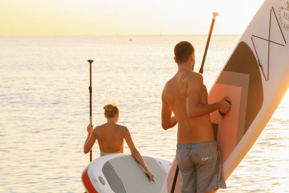 A couple enjoys stand up paddleboarding at sunset on the ocean