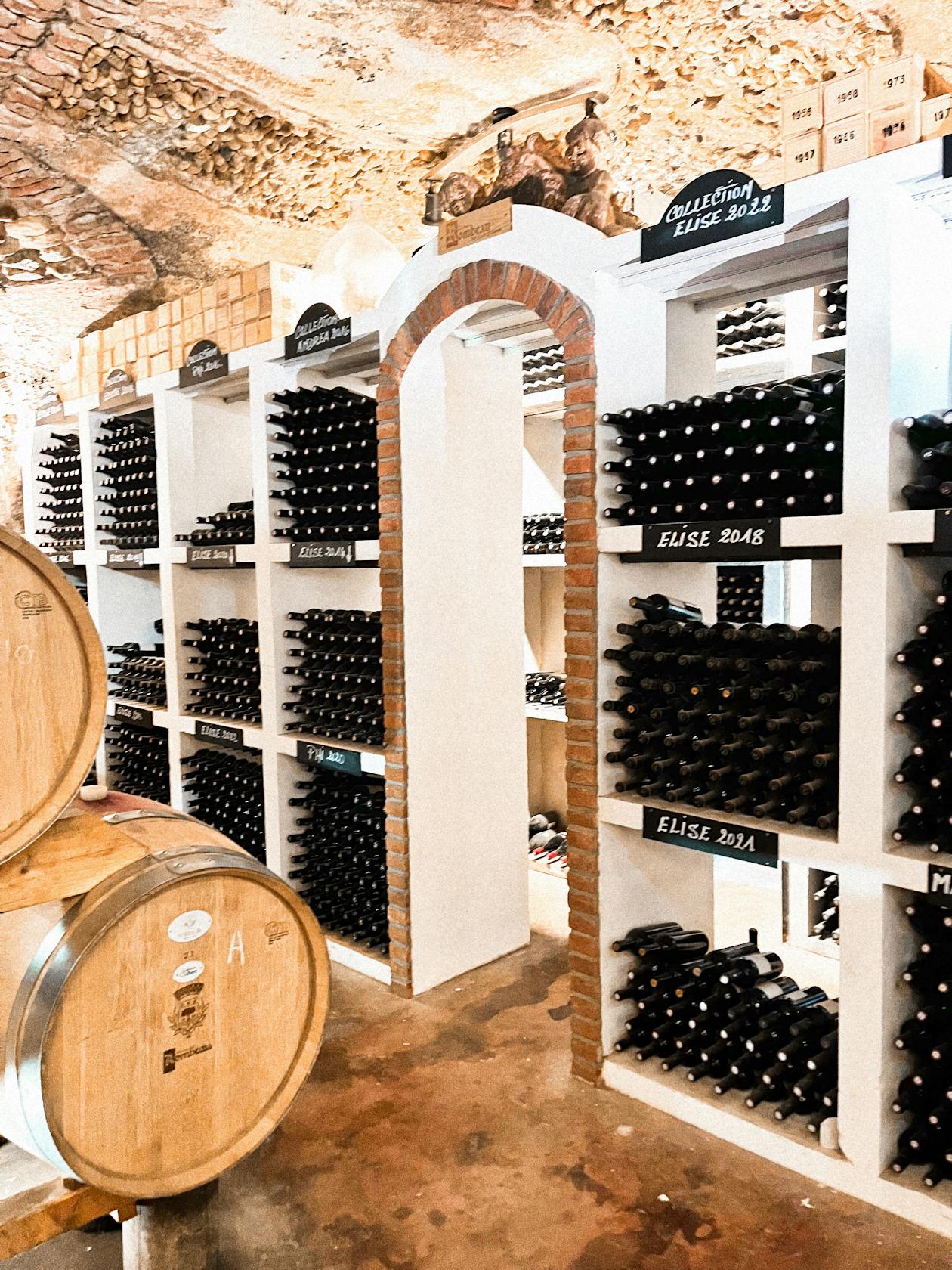 A brick archway leading into a wine cellar filled with bottles and barrels
