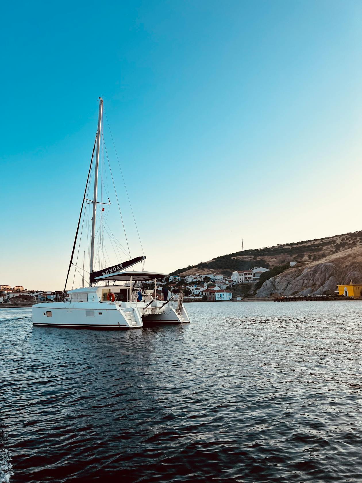 Sailboat cruising along a coastline at sunset with warm golden light on the water