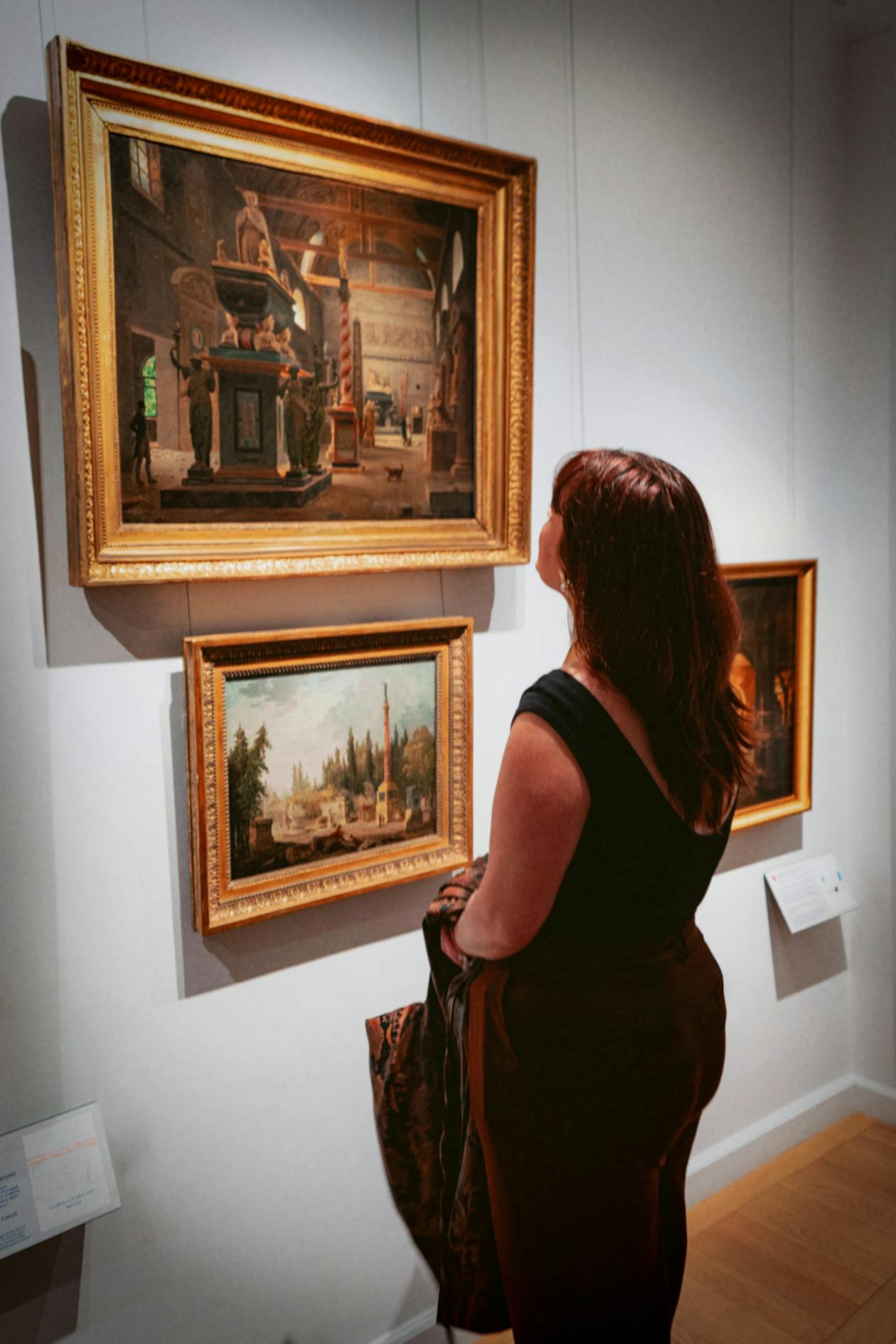 A woman in a Paris gallery observing classical artwork in ornate frames