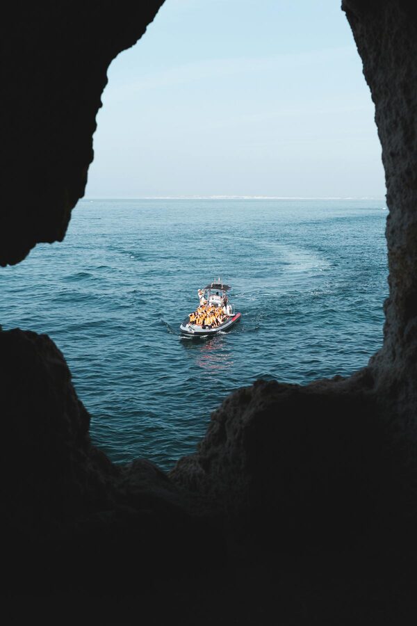 View from inside a sea cave looking out to a boat on the turquoise ocean in Algarve