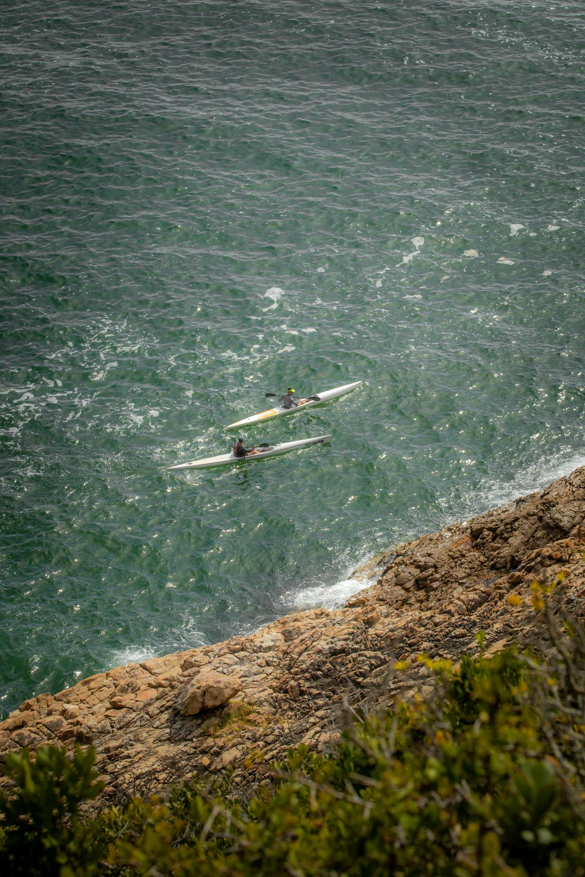Kayakers paddling through clear ocean waters along a rugged rocky coastline
