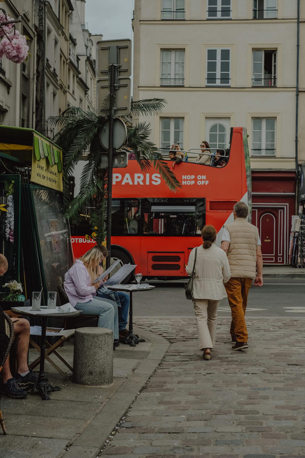 A red hop-on hop-off bus stopped on a Paris street with passengers heading to the top deck