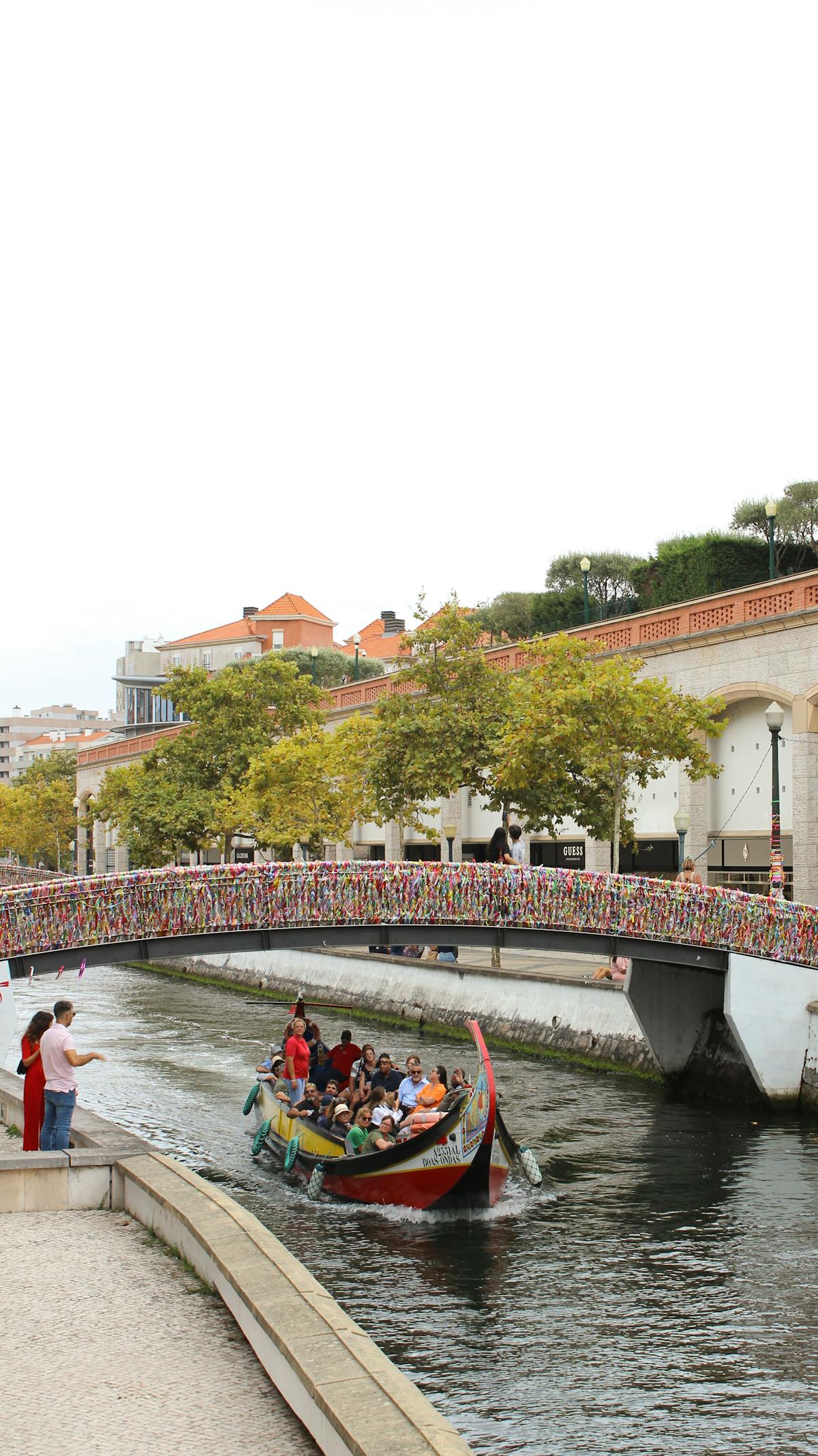 Moliceiro boat gliding under a bridge draped with love locks on an Aveiro canal