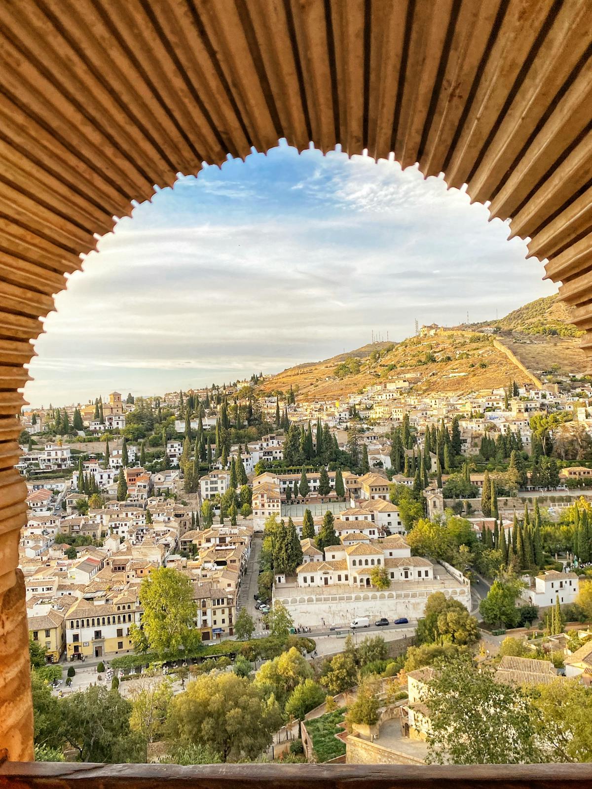 View of Granada cityscape framed through an ornate Alhambra arch with hills and skyline