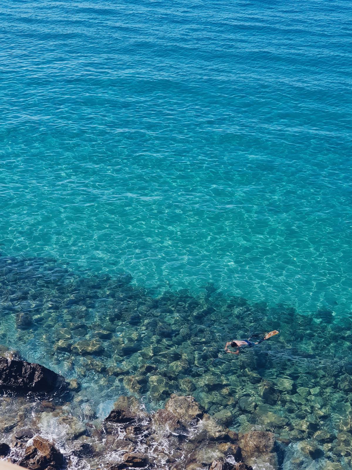 Person snorkeling in clear blue waters above a rocky seabed