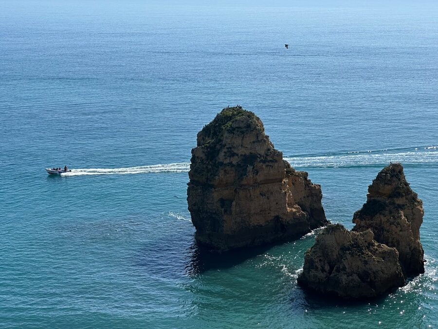 A boat cruising past golden rock formations along the Algarve coastline
