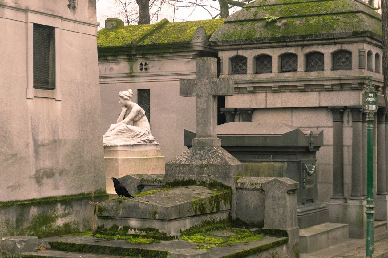 Stone statues and monuments at Pere Lachaise Cemetery in Paris with a crow perched on a tombstone