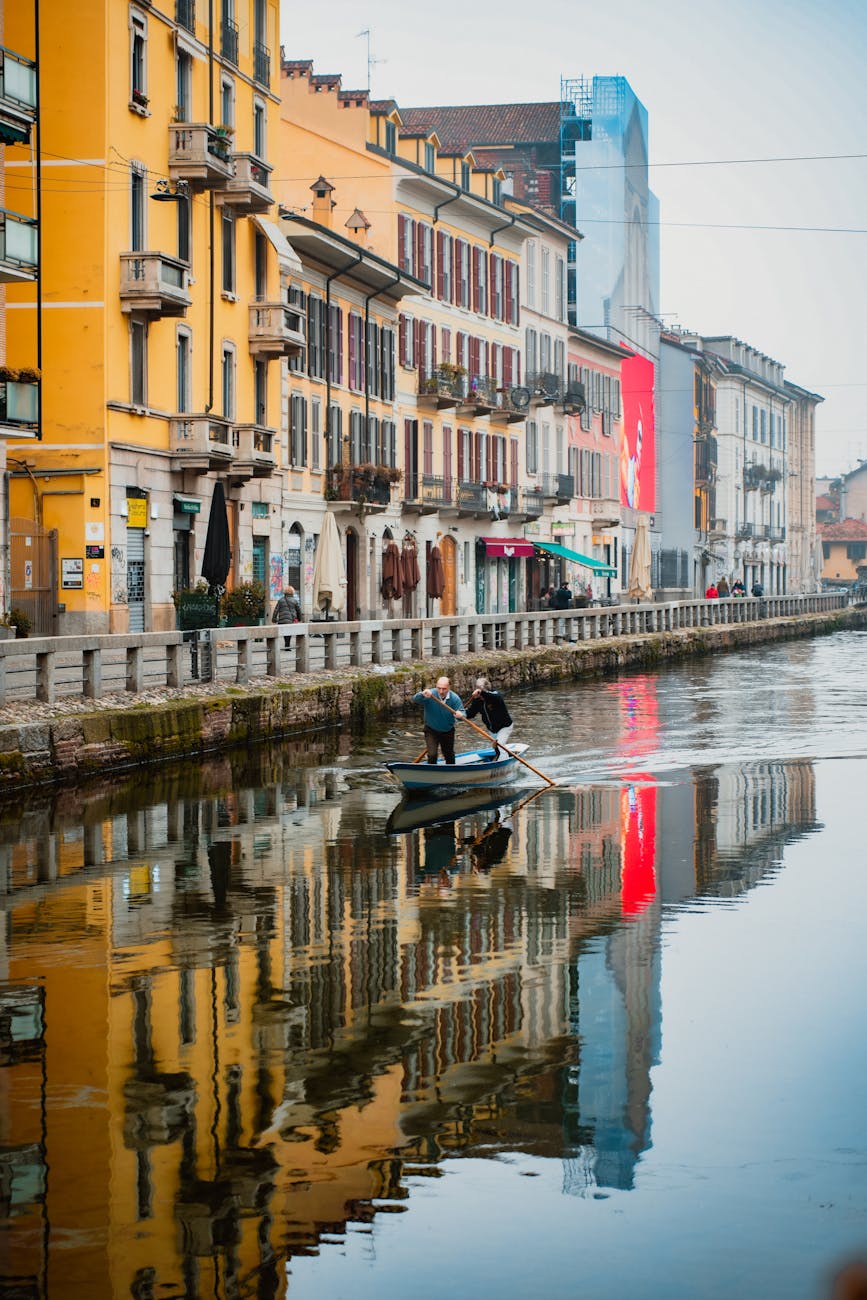 People rowing a boat on the Navigli Canal with colorful building reflections in Milan