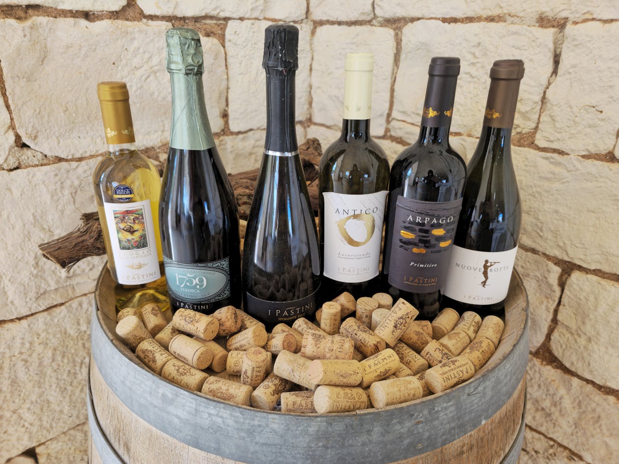 Five wine bottles arranged on a wooden barrel surrounded by loose corks