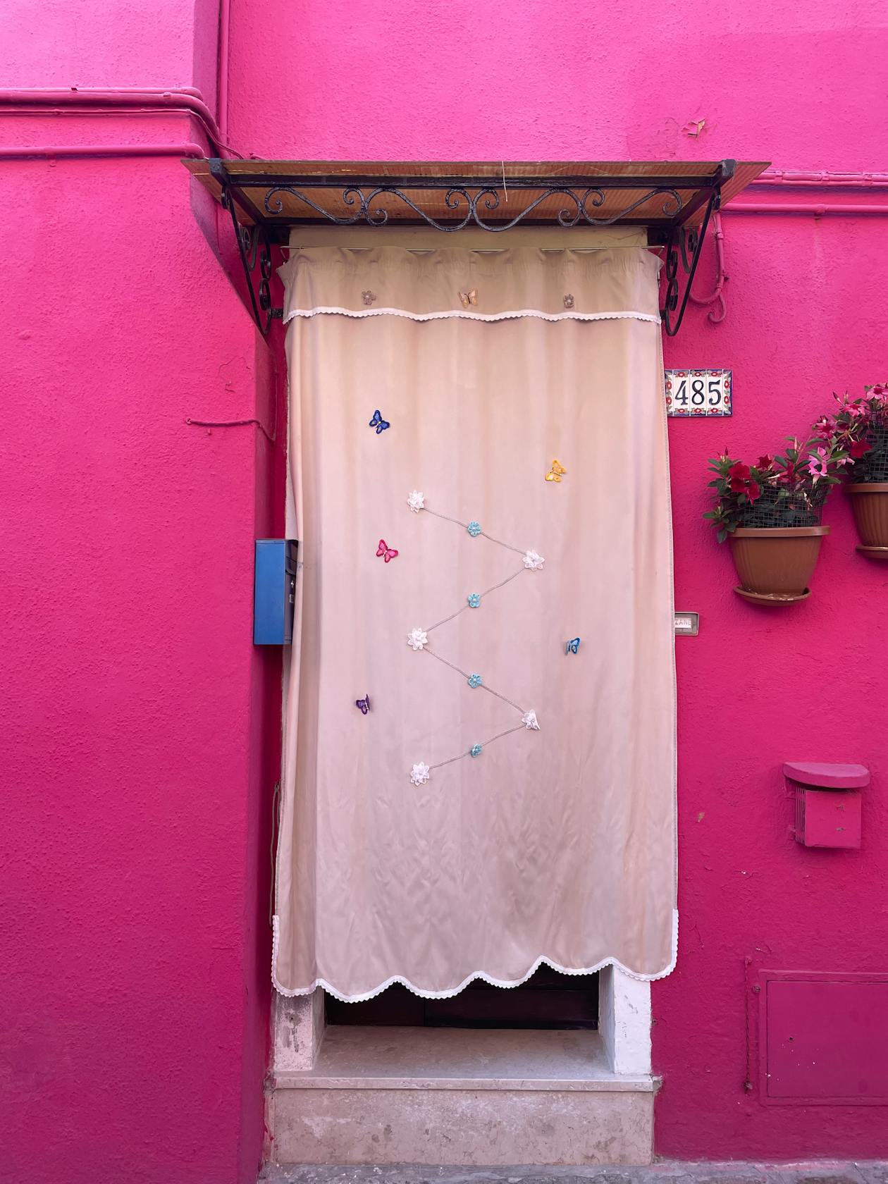 Charming pink house entrance in Burano Italy with decorative curtain and flowers