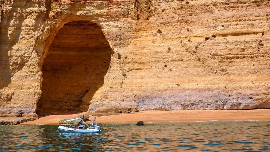 A sightseeing boat cruises near the eroded golden cliffs of the Algarve coast
