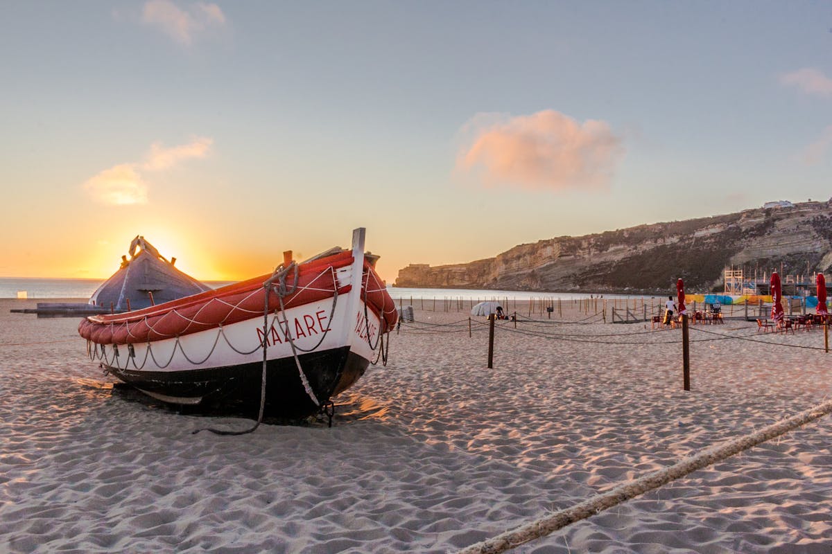 Traditional red and white fishing boat on the sand at Nazare beach in Portugal