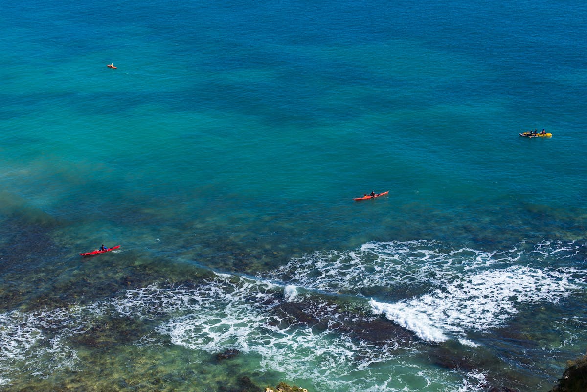 Aerial view of people kayaking on clear blue ocean waters near a rocky coastline