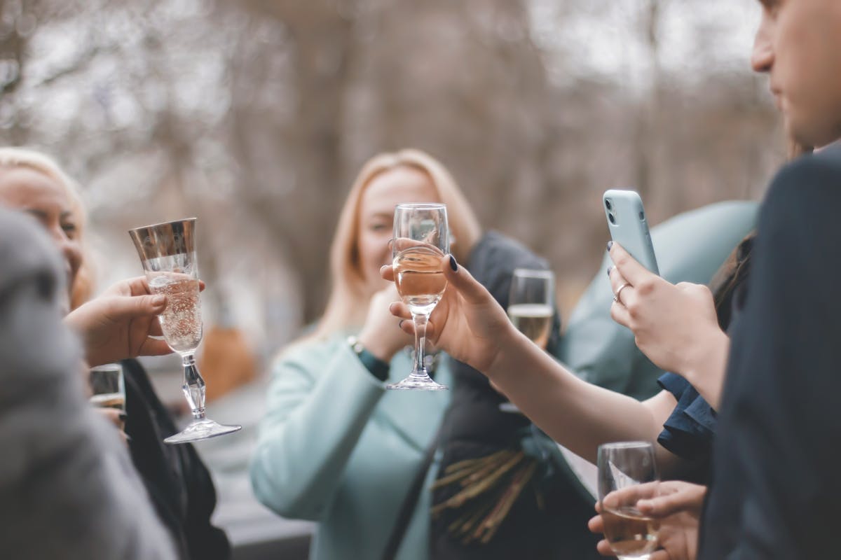A group of friends clinking champagne glasses together outdoors in the sunshine