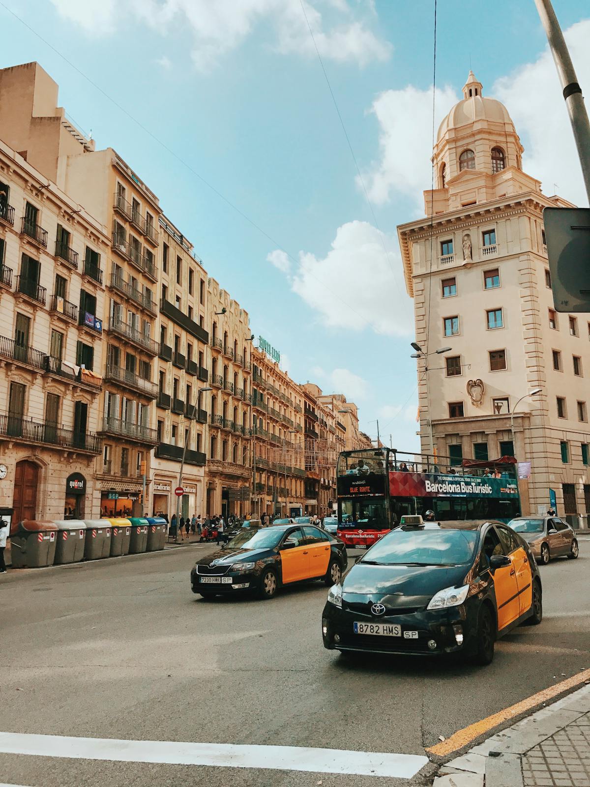 Dynamic street view of Barcelona with taxis buildings and a double-decker bus under a bright sky