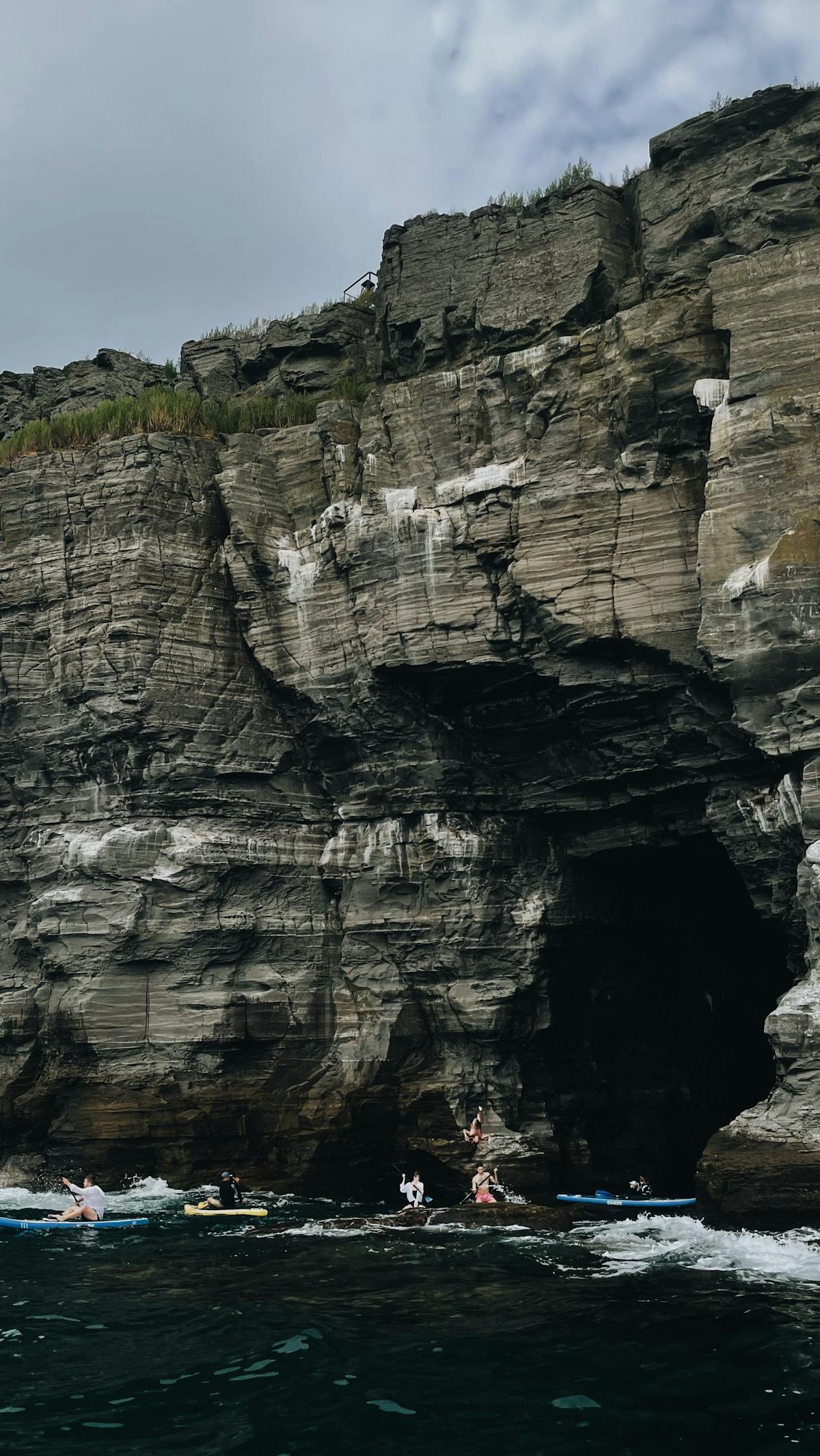 Kayakers exploring dramatic sea cliffs and caves along a rugged coastline