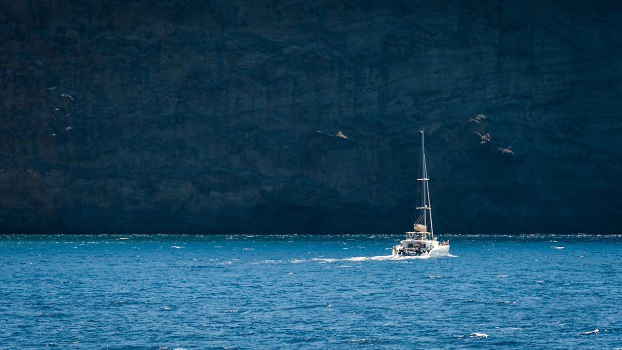 Sailboat sailing through blue Aegean waters near Greek island cliffs