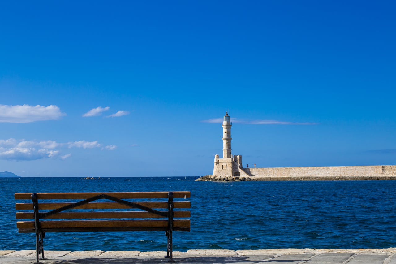 Tranquil scene of the Chania lighthouse with a bench by the sea under a blue sky