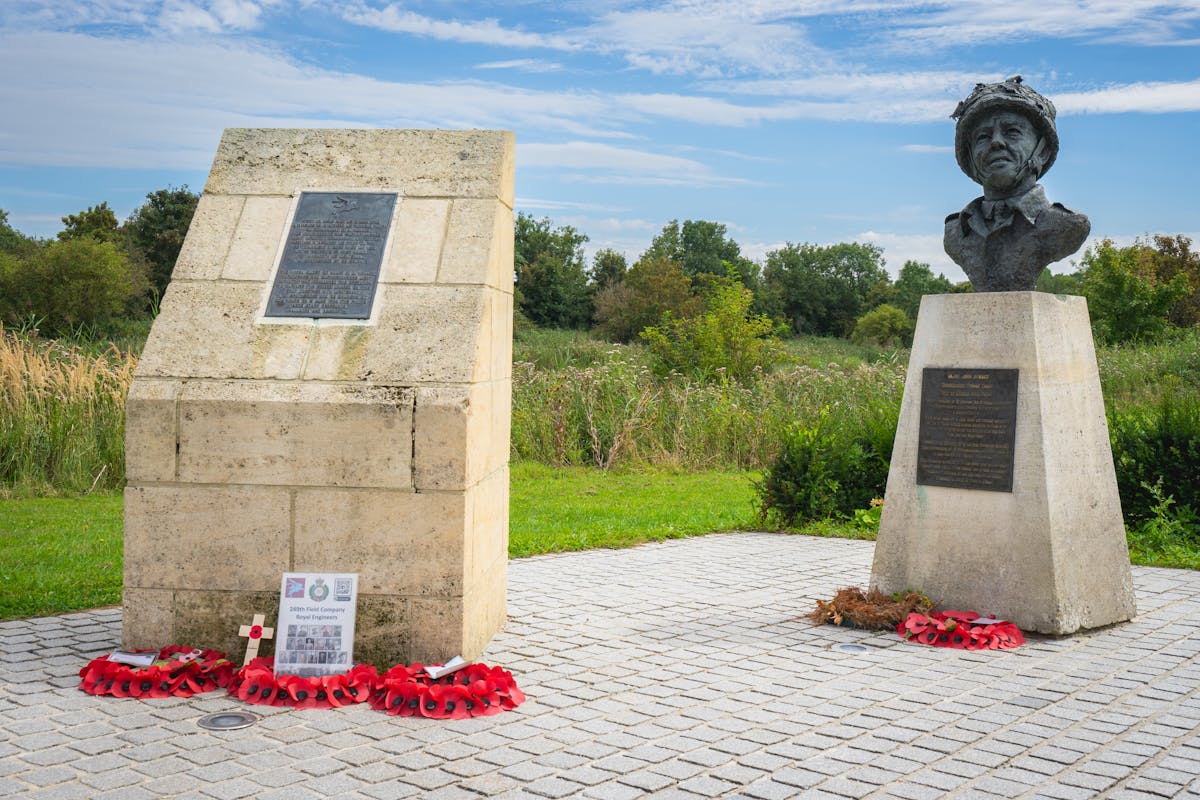 A World War II memorial featuring stone monument and bust surrounded by wreaths in a park