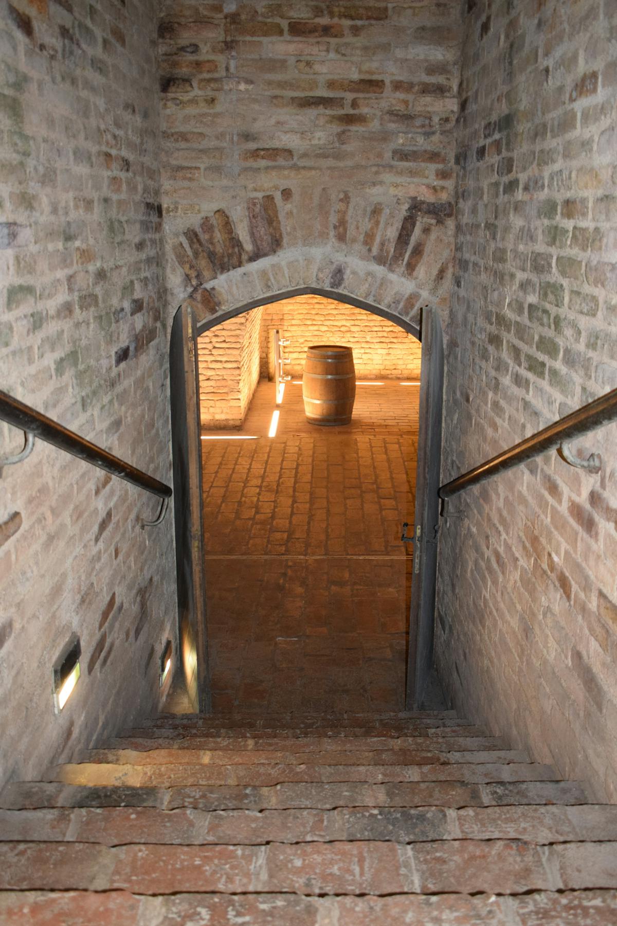 Historic brick corridor with arch doorway leading to a cellar with a wooden barrel