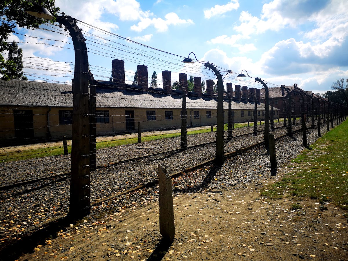 Barbed wire fence at a historical concentration camp with barracks in background