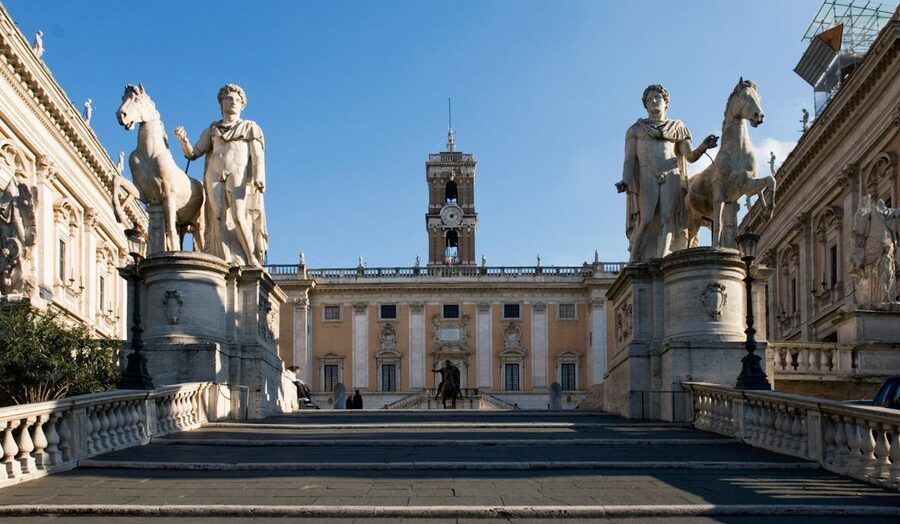 Statues and visitors at Capitoline Hill in Rome under summer sunlight with Renaissance architecture
