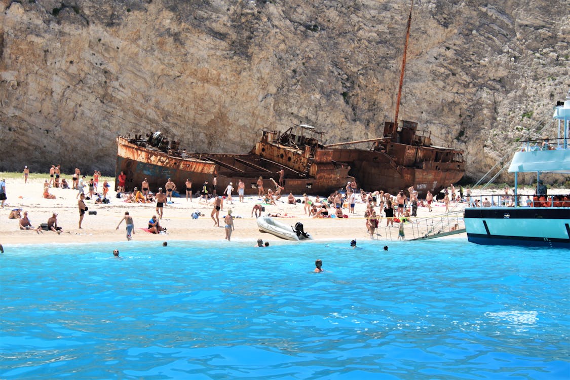 Tourists walking around the shipwreck on Navagio Beach with turquoise sea in the background