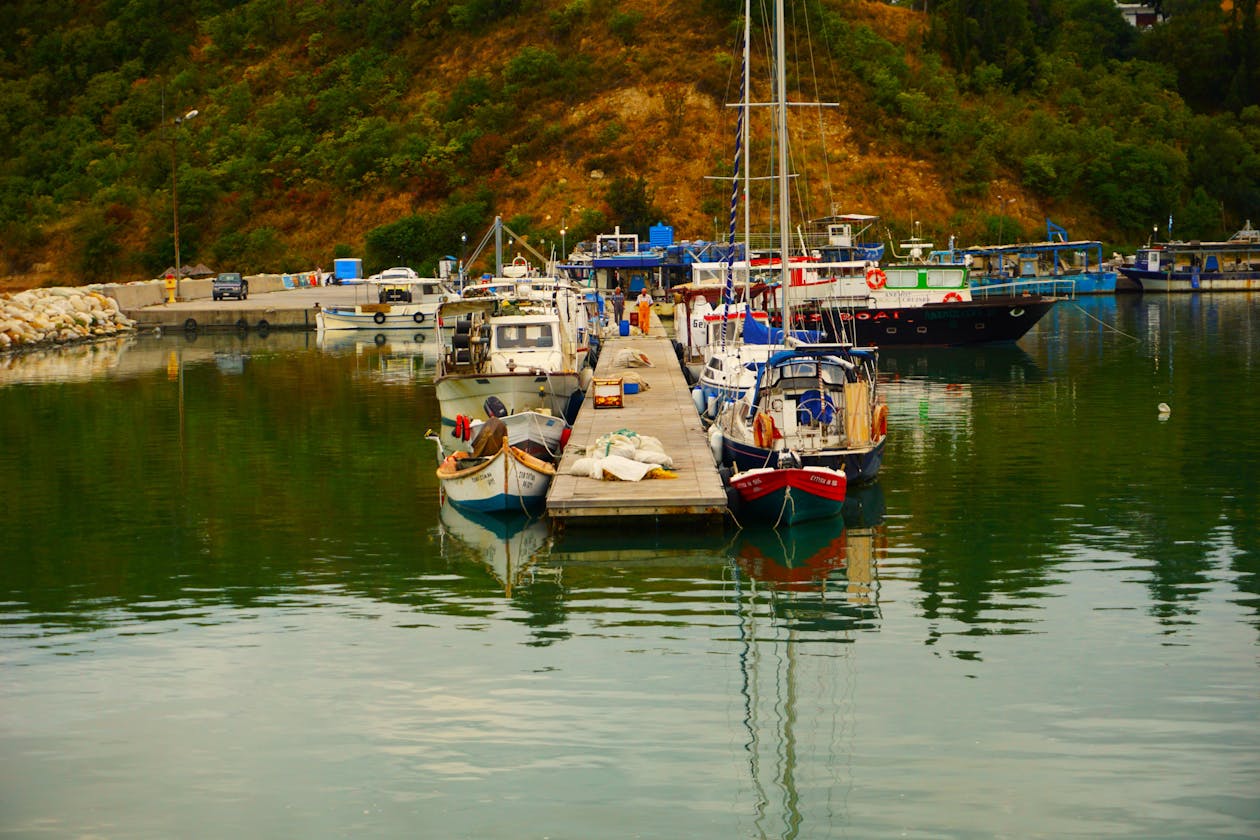 Wooden boats tied up at a pier in a quiet Greek harbor with lush hillsides