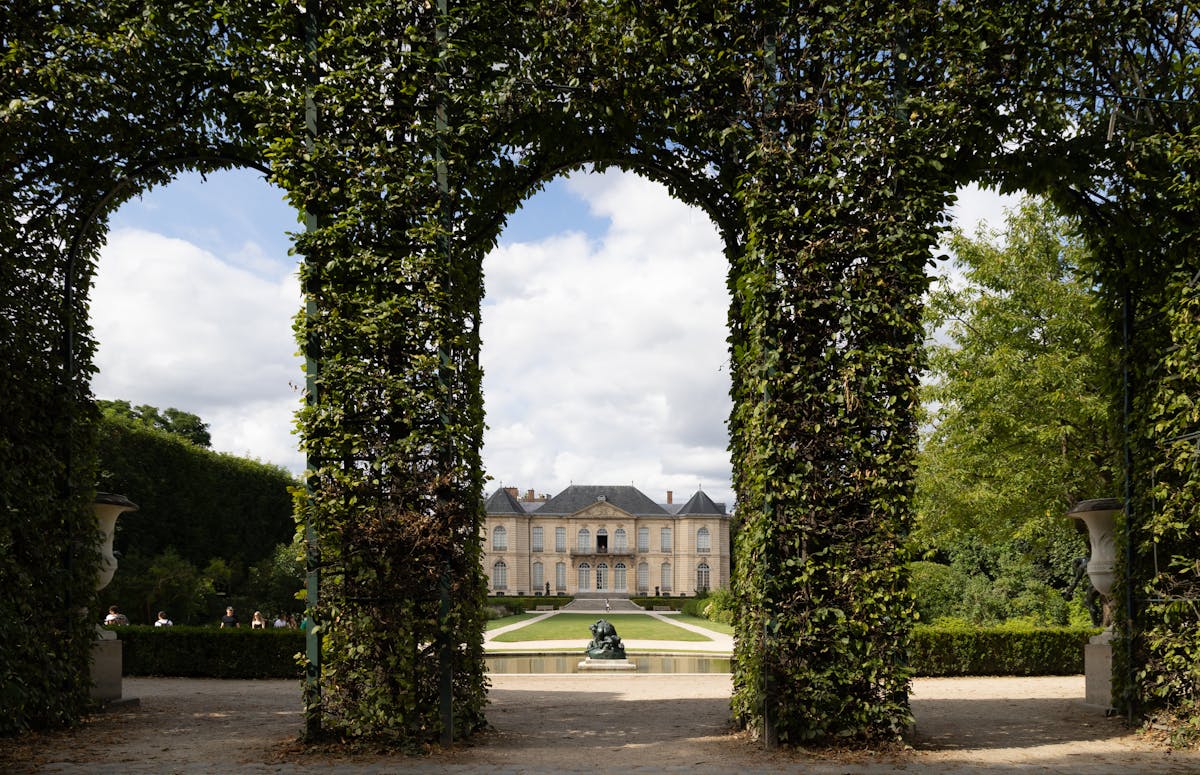 View of the Hotel Biron through a lush green garden archway at the Rodin Museum