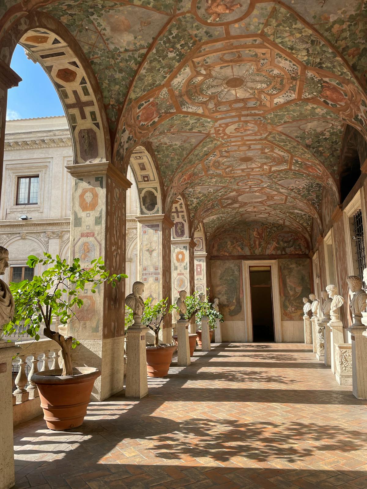 Sunlit Renaissance courtyard with marble busts and arched architecture in Rome