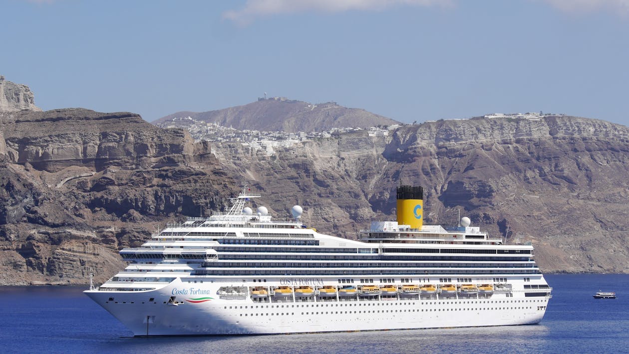 A cruise ship sailing past dramatic cliffs of a Greek island under clear blue skies