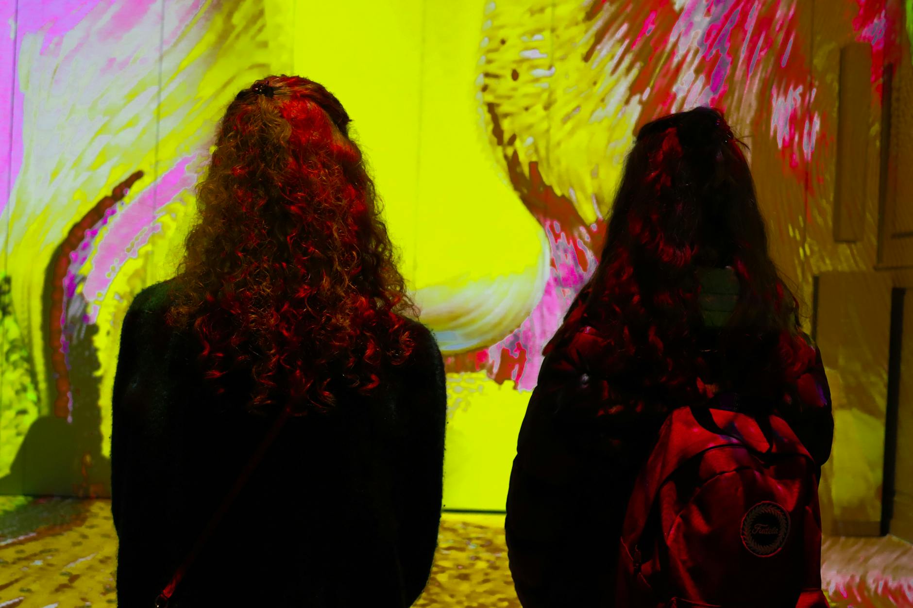 Two visitors with backpacks looking at large-scale digital art projected on walls in a museum