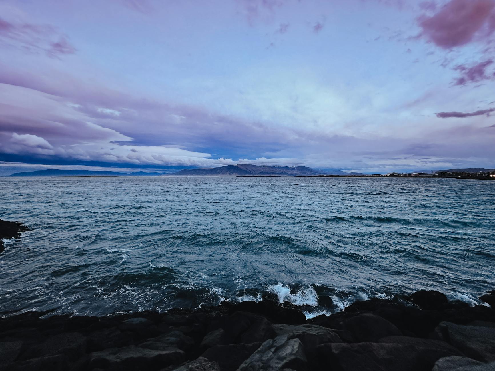 Dramatic dusk scene of Reykjavik coastline with colorful sky and ocean