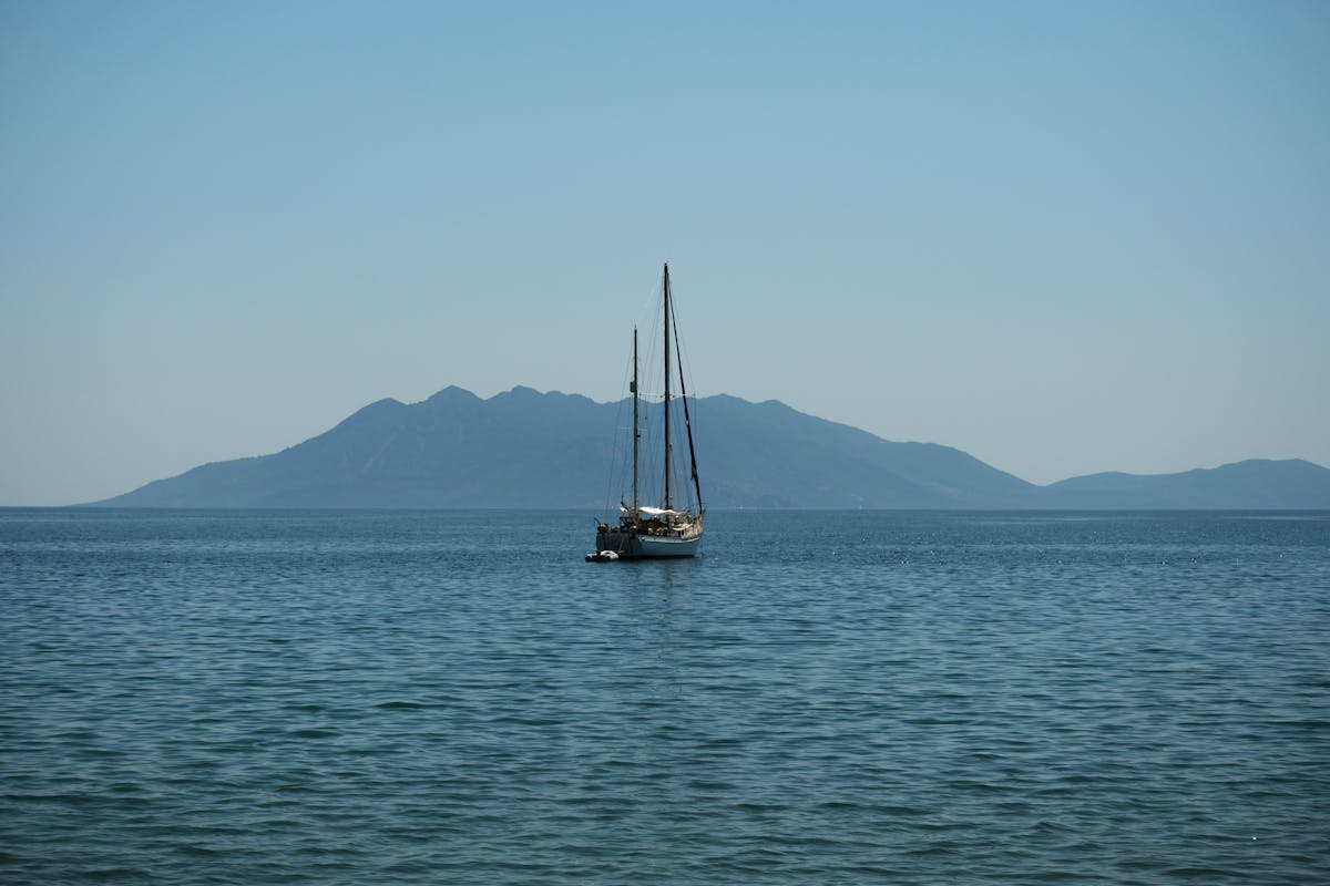A sailboat drifting near a green island under clear blue skies