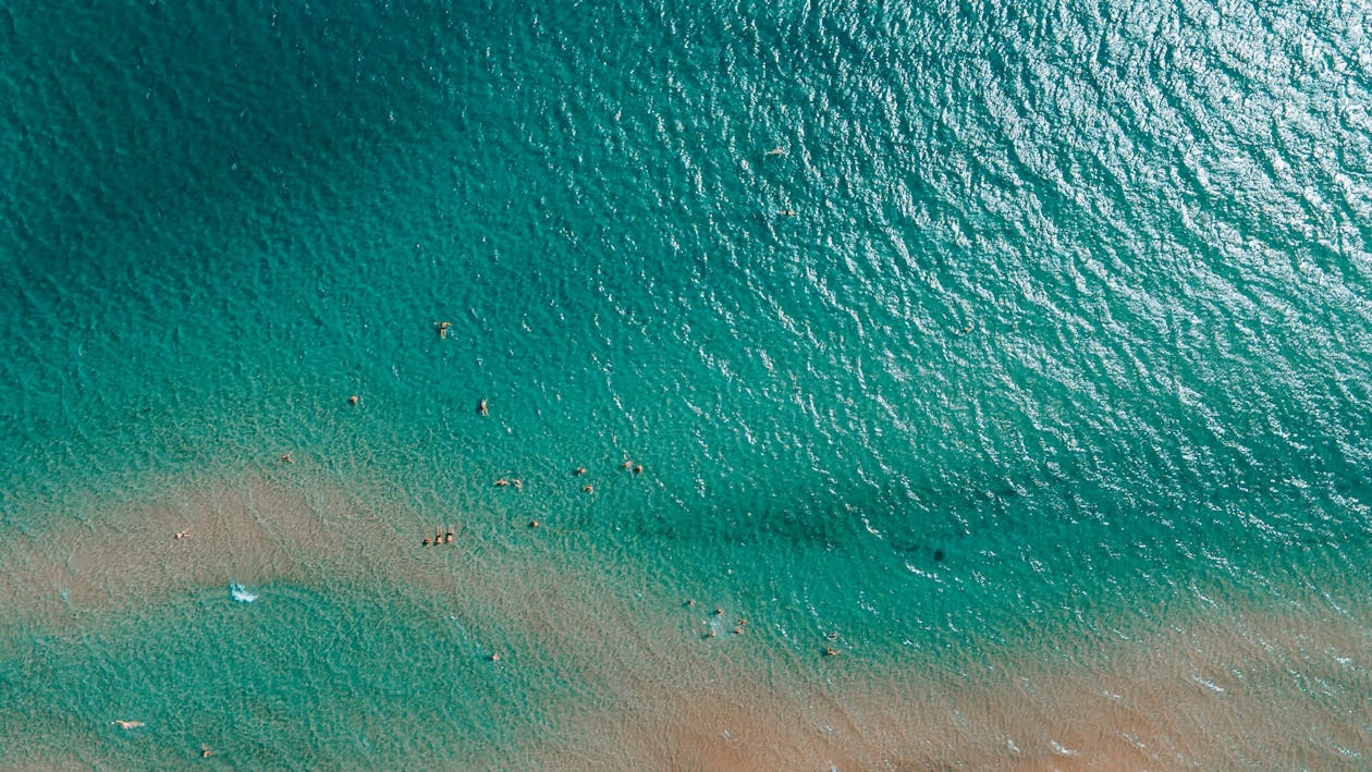 Drone shot of people swimming in bright turquoise waters near a Greek beach