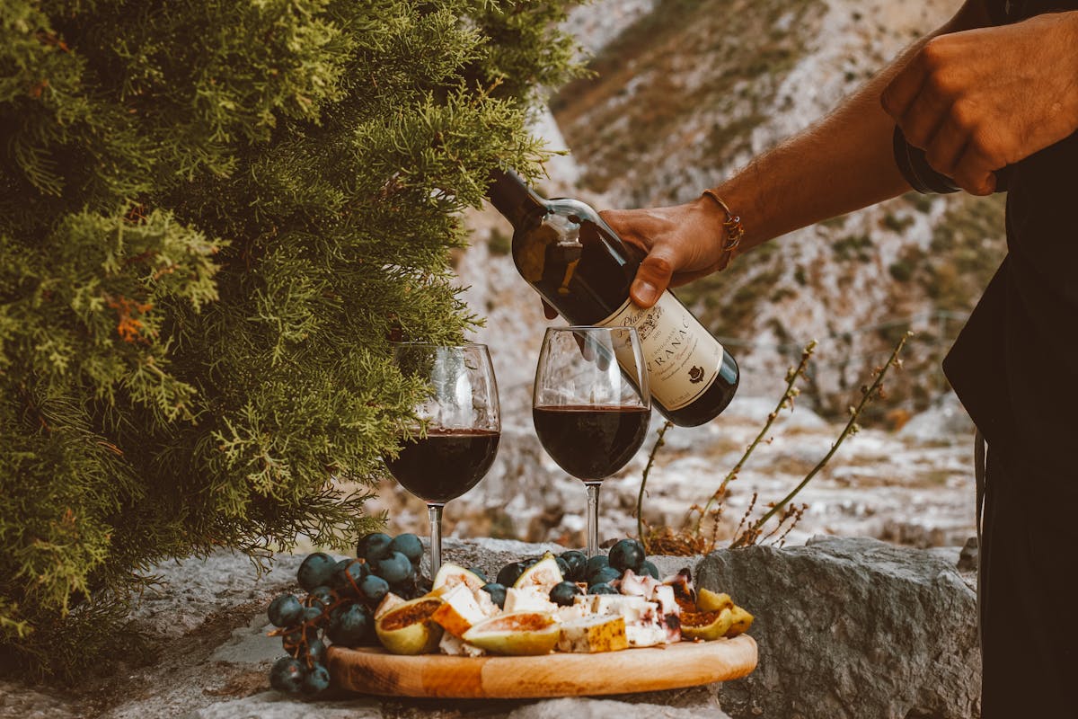 Wine, cheese, and grapes arranged on a stone surface outdoors
