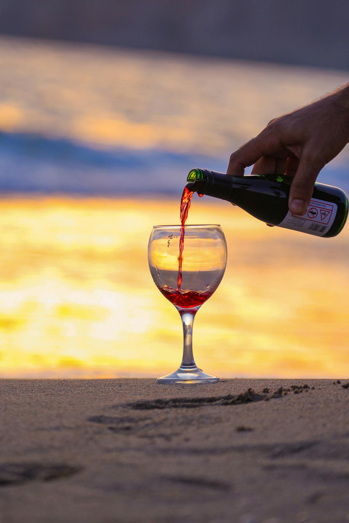 Red wine being poured into a glass at sunset on a beach