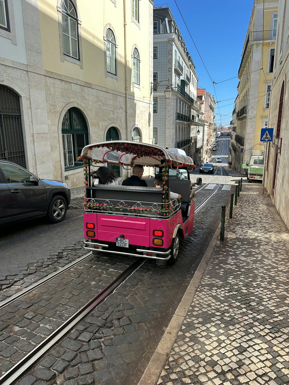 Pink tuk-tuk driving through Lisbon's cobblestone streets with traditional Portuguese buildings on both sides