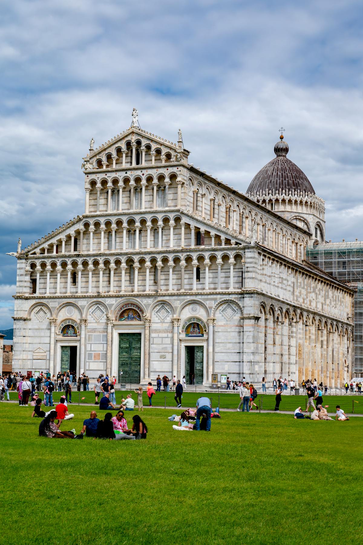 Pisa Cathedral with visitors relaxing on the green lawn on a sunny day