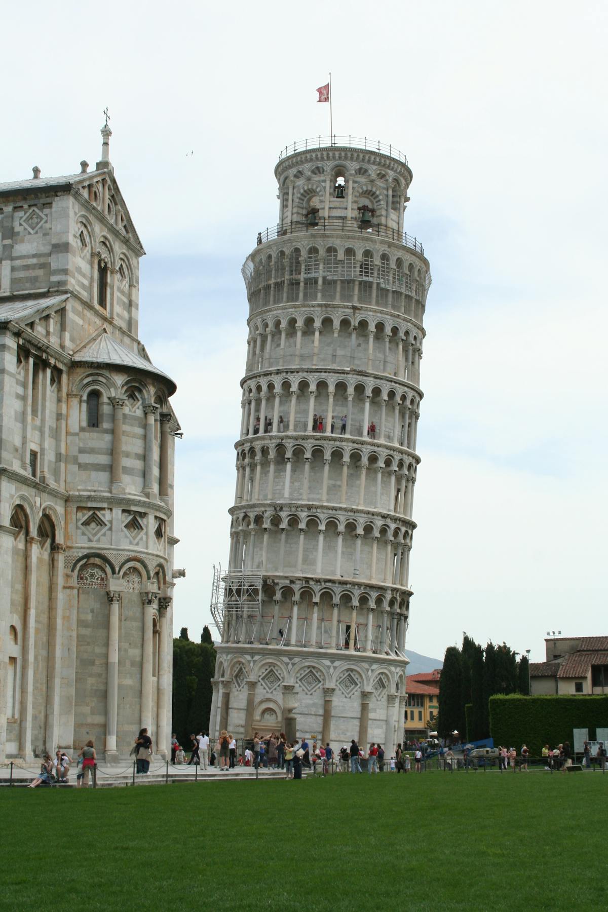 Wide view of the Leaning Tower of Pisa with travelers scattered across the green lawn