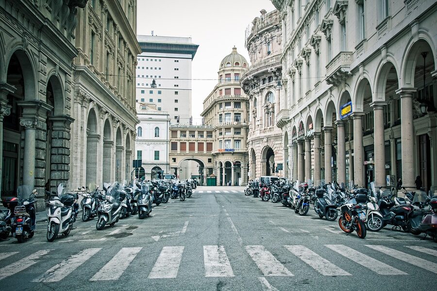 A scooter parked on a narrow street in Genoa with Italian urban architecture in the background