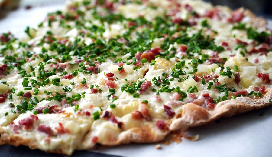 Traditional Alsatian flammekueche tarte flambee with onions and bacon on a wooden board