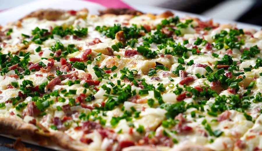 A freshly baked tarte flambee topped with cheese served on a rustic surface