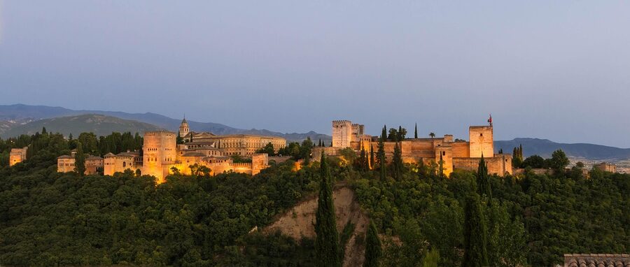 Wide panoramic view of the Alhambra complex at dusk with the city of Granada spread below