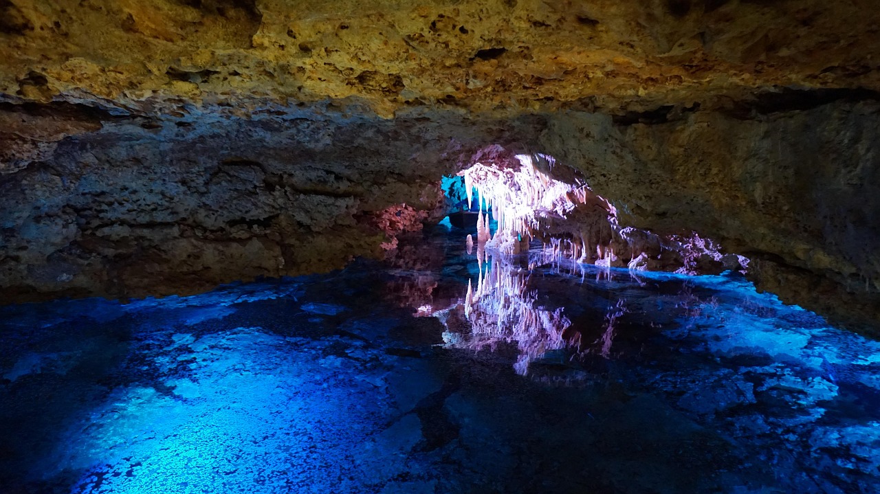 Underground cave lake illuminated by colored lights with stalactites hanging from the ceiling