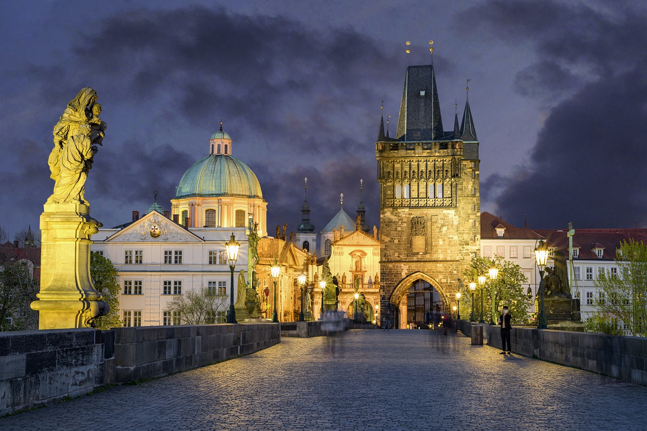 Charles Bridge at dusk with statues along the railings and Prague Castle illuminated in the background